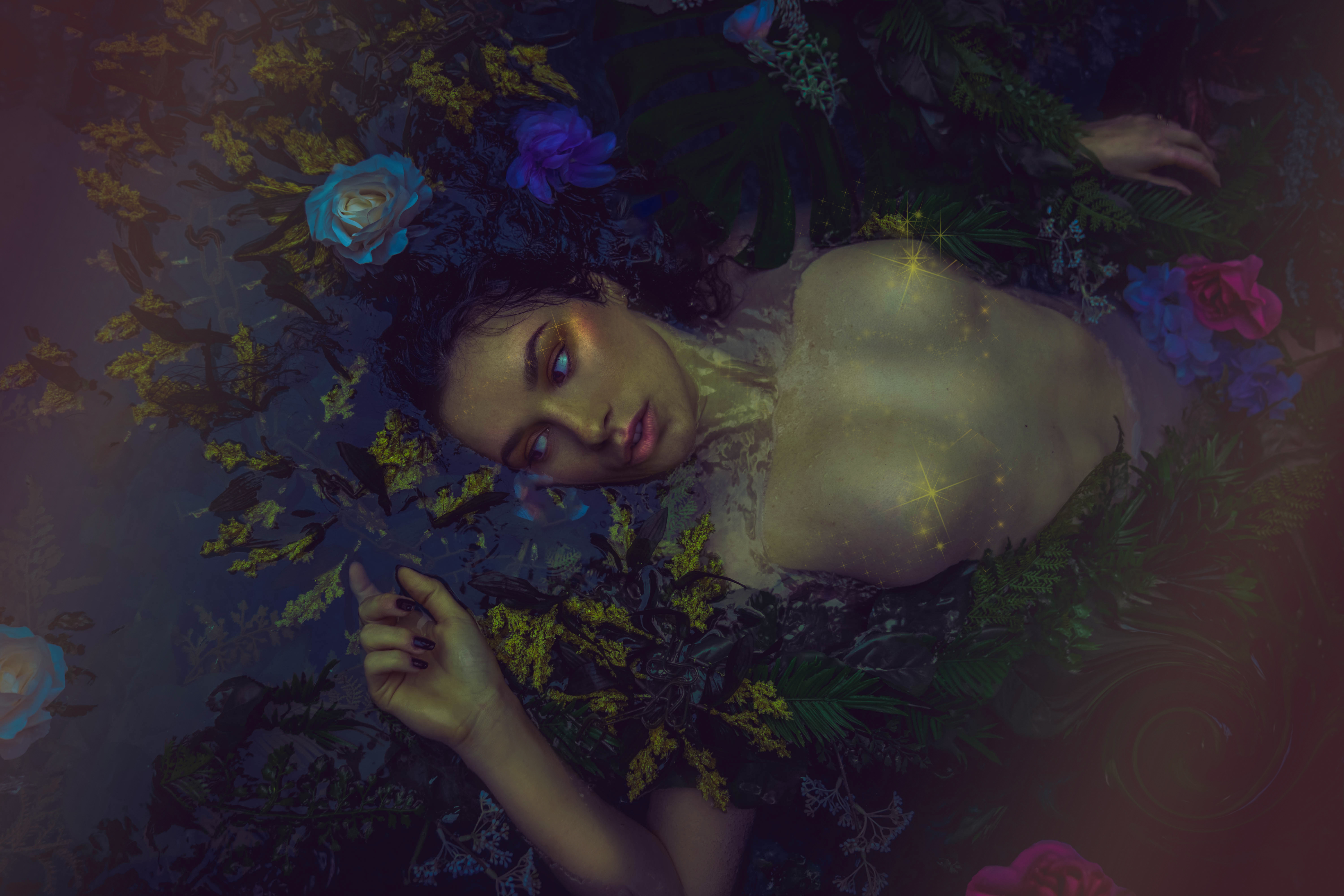 photograph of a woman floating in water surrounded by flowers, vines, and leaves. inspired by the painting ophelia by sir john everett millais
